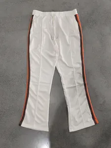 Full length flat lay view of cream flared sports pants with orange and brown side stripes.