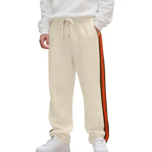 Close-up detail of men's cream flared sweatpants featuring contrast orange side stripes.