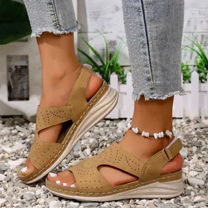 Close-up van beige platte sandalen met ajourpatroon, gedragen op een natuurlijke grindvlakte.