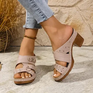 Close-up of beige peep-toe block heel mules with cutout patterns and chunky sole.