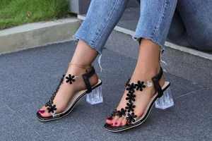 Detailed view of women's transparent block heel sandals featuring elegant black floral motifs
