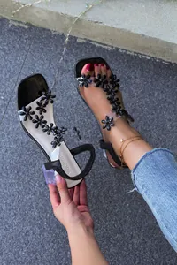 Detailed view of floral Roman sandals with clear crystal block heels on pavement