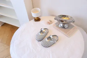 Élégantes sandales tressées argentées pour filles sur une table blanche minimaliste