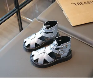 Primer plano de sandalias romanas plateadas para niñas con correas cruzadas y hebillas.