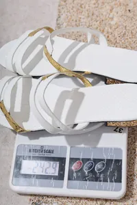Detailed view showing the weight of these white snakeskin flat sandals on a scale