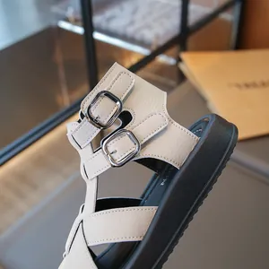 Sandalias romanas beige para niña con hebillas plateadas y suela negra gruesa.