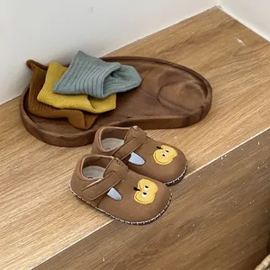 Primer plano de zapatos de bebé marrones con bordado de manzana y suela blanda para caminar.