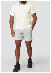 Ganzkörperansicht eines Mannes in einem cremefarbenen Golf-Poloshirt und grauen Shorts.