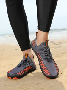 Graue Outdoor-Wasserschuhe mit orangefarbenem 'OUT DOORS' Druck auf Sandstrandhintergrund