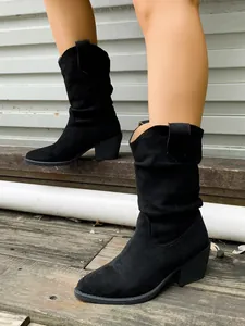 Vue détaillée des bottes western plissées en daim noir à bout pointu sur un sol en bois