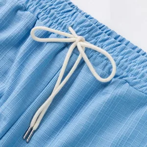 Gros plan de la taille élastique avec cordon blanc sur un pantalon bleu clair texturé.