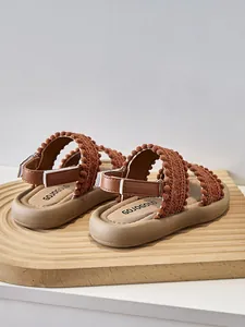 Vista detallada de sandalias étnicas para niñas con correas de pompones y suelas blandas.