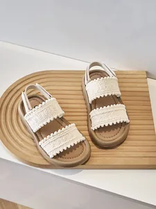 Vista detallada de sandalias étnicas para niñas con pompones en bandeja de madera