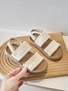 Primer plano de sandalias étnicas para niña con tiras tejidas, pompones y suelas blandas