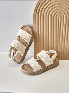 Primer plano de sandalias étnicas para niña con correas tejidas y adornos de pompones.