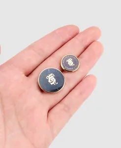 Close-up of navy blue and gold enamel buttons with crest and International text on a hand