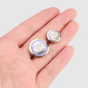 Élégants boutons en émail cloisonné violet avec blason doré tenus dans la paume de la main