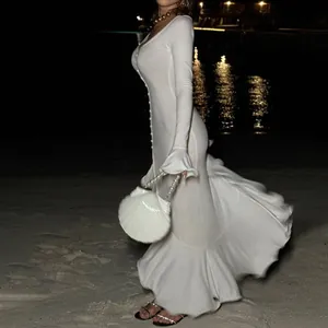 Detail view of an elegant white long sleeve V-neck ruffled dress on a night beach