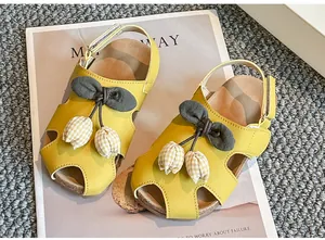 Detailansicht gelber Mädchensandalen mit Tulpen-Anhängern aus Stoff und Schleife.