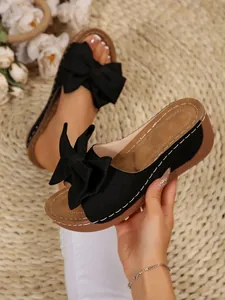 Detailed view of black women's wedge slippers featuring a stylish large bow
