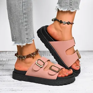 Detailed view of stylish pink platform slides featuring double gold buckle straps on feet.