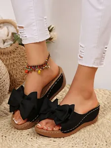 Detail view of black platform wedge slippers with large bows and white stitching accents