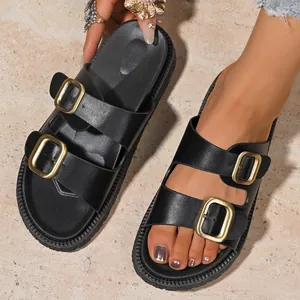 Macro view of black platform sandals with shiny gold double metal buckles and thick sole.