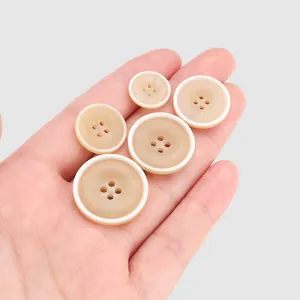 Hochwertige beige Harzknöpfe mit weißem Rand für Hemden und Mäntel in der Hand