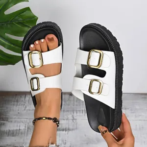 Close-up of white platform sandals with gold double buckle straps on foot and hand
