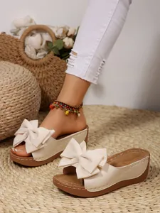 Close-up detail of stylish cream wedge slippers featuring a large fabric bow design