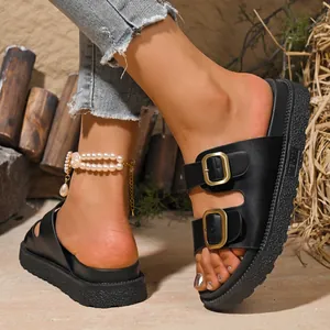Close-up detail of black platform slides with double gold buckles on leather straps