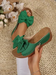Close-up of stylish green platform slippers for women featuring a large decorative bow