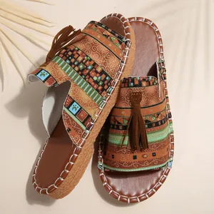 Detailansicht der flachen Ethno-Sandalen mit braunen Quasten und Kontrastnähten.