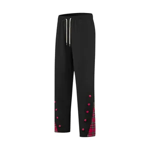 Dettaglio dei pantaloni neri da uomo con orlo scozzese rosso e bottoni rosa decorativi.
