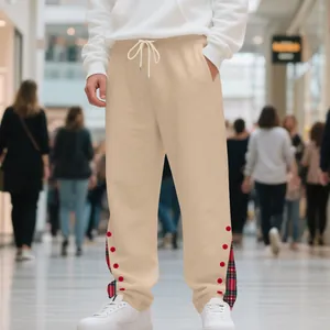Dettaglio dei pantaloni sportivi beige da uomo con orlo scozzese e bottoni rossi.