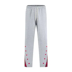 Dettaglio dei pantaloni sportivi grigi da uomo con bottoni rossi e inserti in tessuto scozzese