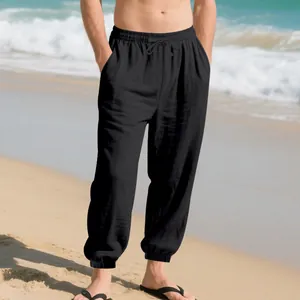 Men's loose linen drawstring joggers with elastic cuffs shown in a beach setting