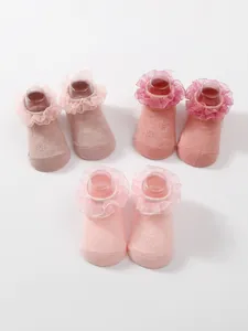 Detailed view of three pairs of pink baby ruffled socks with lace trim and foot forms