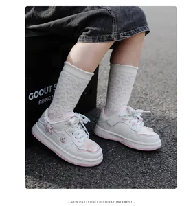 Detaillierte Ansicht weißer Mädchen-Sneaker mit rosa Rand und bunten Pompons an den Schnürsenkeln