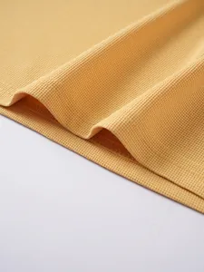 Close-up detail of yellow waffle knit fabric and hem stitching of a men's polo shirt