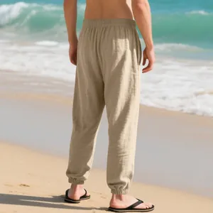 Men's loose khaki linen joggers shown from back view on a tropical summer beach