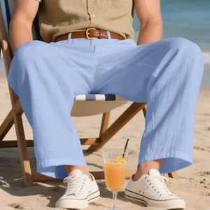 Vue détaillée d'un pantalon en lin bleu clair porté par un homme sur une plage.