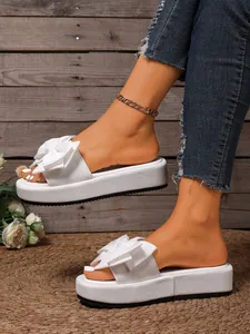 Detalle lateral de zapatillas de plataforma blancas con lazo grande y tejido texturizado