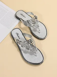 Detalle de chanclas plateadas con adornos florales brillantes y suela blanda.