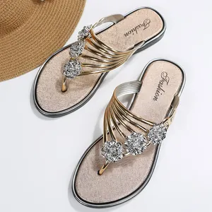 Vista detallada de chanclas de mujer con flores de strass plateadas y correas doradas.