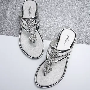 Primer plano de sandalias de dedo plateadas con elegantes flores de pedrería y acabado metálico.