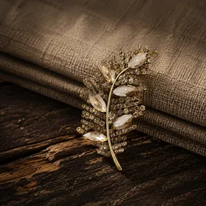 Primer plano de broche de hoja con diamantes champán sobre fondo de madera y lino vintage.