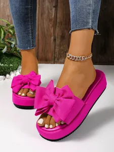 Vista detallada de las sandalias con plataforma fucsia con un lazo decorativo grande.