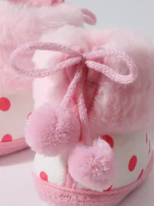 Nahaufnahme von rosa Baby-Winterstiefeln mit flauschigen Pompons und roten Punkten
