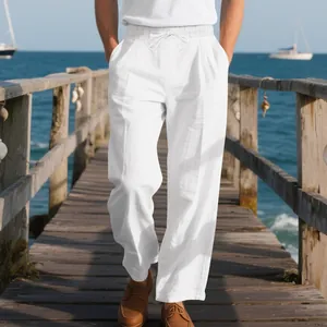 Detail of men's loose white linen beach trousers worn on a sunny coastal wooden pier